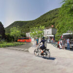 Vue en perspective d'une petite gare de territoire rural avec une piste cyclable, un bus, des commerces de proximité et des transports en commun